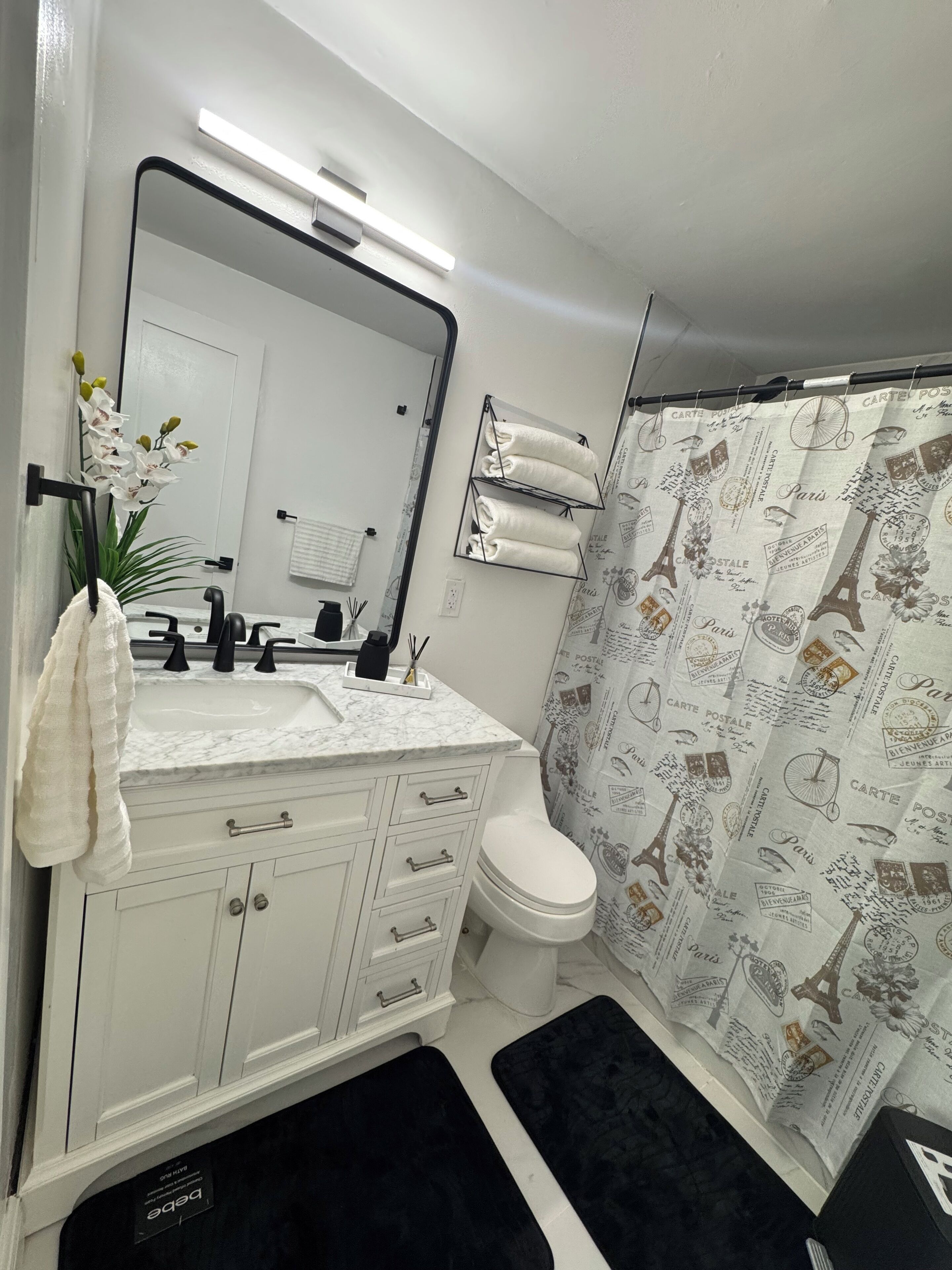 Une salle de bain avec un meuble-lavabo blanc, un miroir, un évier, des toilettes et un rideau de douche orné de motifs sur le thème de Paris.