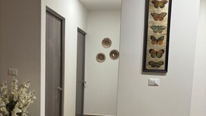 Een moderne hal met een houten deur, een donkergrijze stoel, een eettafel met een geweven placemat en een wanddecoratie van een vlinder.