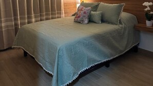 Een slaapkamer met een bed, een kruis aan de muur en een ingelijst beeld boven het bed.