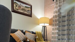 Een woonkamer met een bank, gekleurde kussens, een lamp, een vloerkleed en een aan de muur hangend kunstwerk.