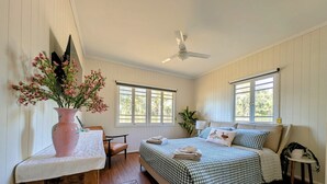 A bedroom with a bed, a chair, a table with a vase of flowers, and a ceiling fan. - Scenic Rim Farmstead Retreat, Rathdowney (Rathdowney)