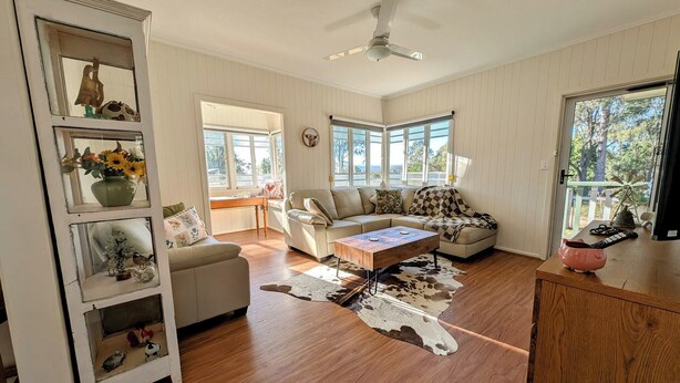 A spacious living room with a sofa, a coffee table, and a wooden cabinet. There is a window with blinds, a ceiling fan, and a view of the outdoors. - Scenic Rim Farmstead Retreat, Rathdowney (Rathdowney)
