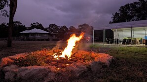 A campfire in a natural setting with a covered outdoor area in the background. - Scenic Rim Farmstead Retreat, Rathdowney (Rathdowney)