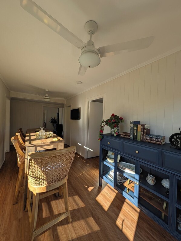 A dining area with a wooden table and chairs, a ceiling fan, and a blue console table with books and a clock. - Scenic Rim Farmstead Retreat, Rathdowney (Rathdowney)