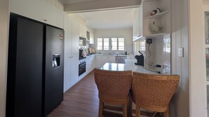 A modern kitchen with white cabinetry, a black refrigerator, a dining area with two wicker chairs, and a window providing natural light. - Scenic Rim Farmstead Retreat, Rathdowney (Rathdowney)