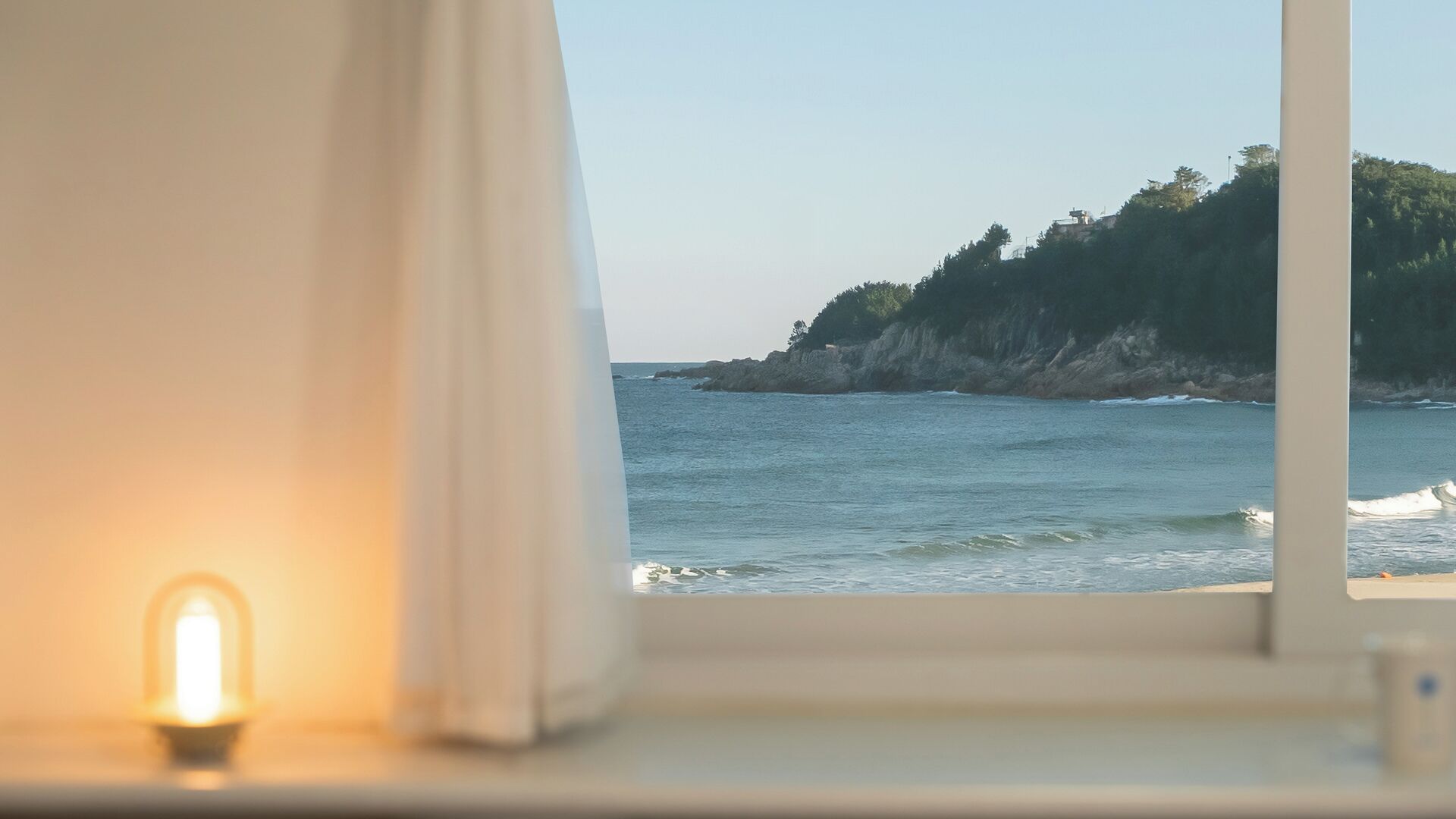 A window with a view of the sea and a rocky coastline.