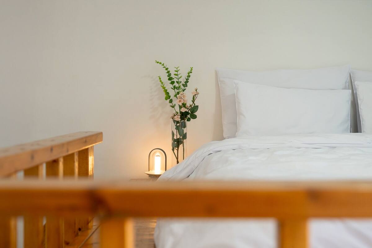 A neatly made bed with white linens, a bedside table with a lamp, and a vase with flowers.