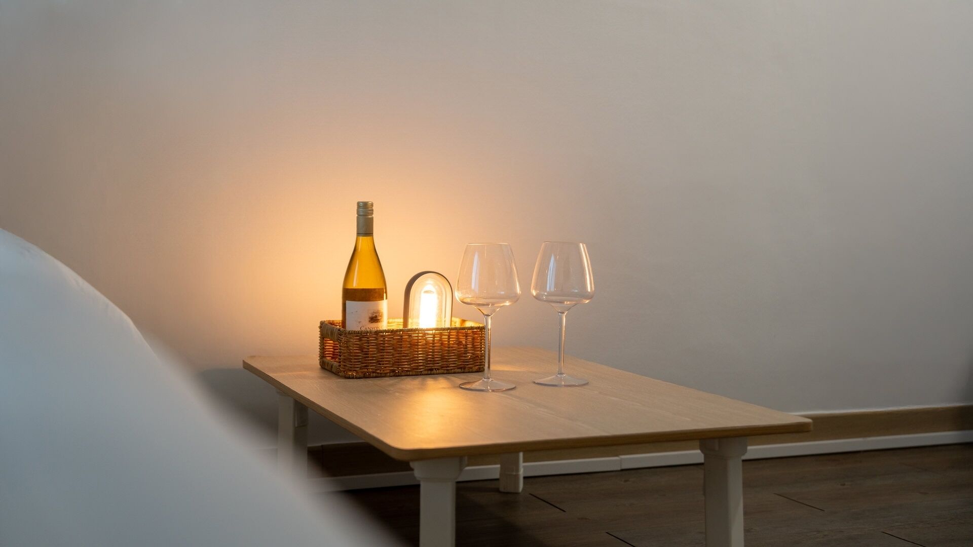Una mesa con una botella y dos vasos, una cesta de mimbre y una fuente de luz.