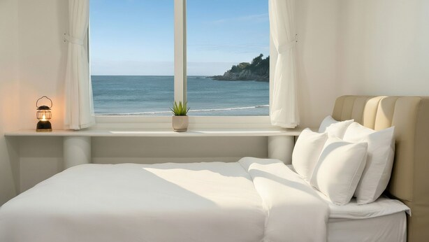 Un dormitorio con cama, ventana con cortinas, planta en maceta y una luz nocturna.