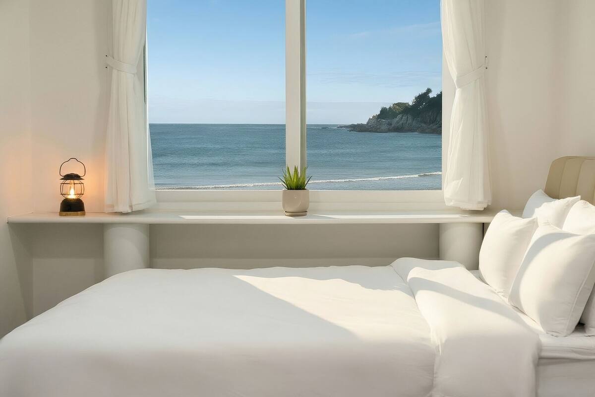 A bedroom with a bed, a window with curtains, a potted plant, and a nightlight.