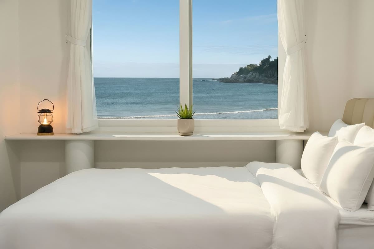 Un dormitorio con cama, ventana con cortinas, planta en maceta y una luz nocturna.