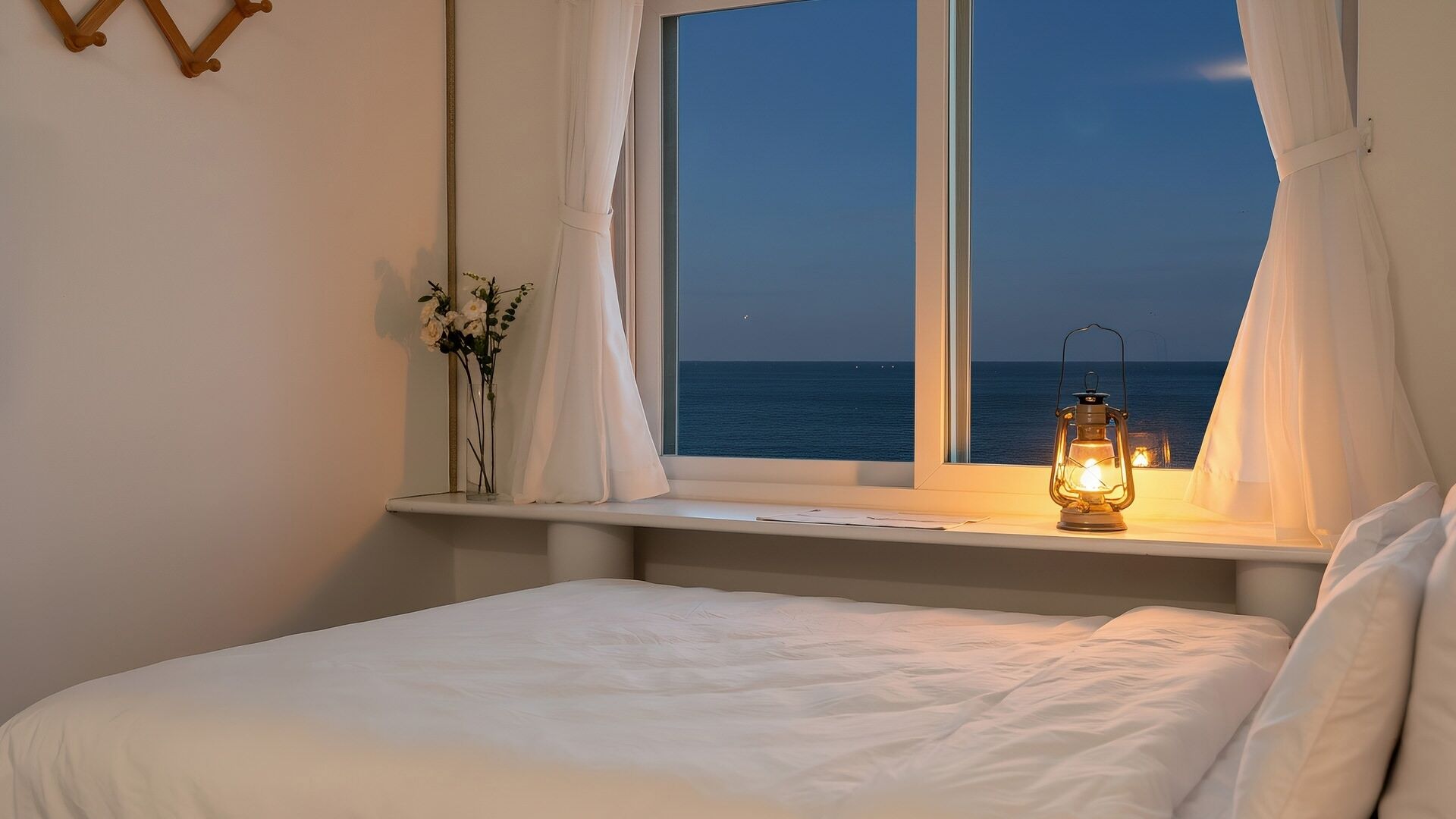 Un dormitorio con cama, ventana con vista al mar, luz nocturna y un florero con flores sobre una estantería.