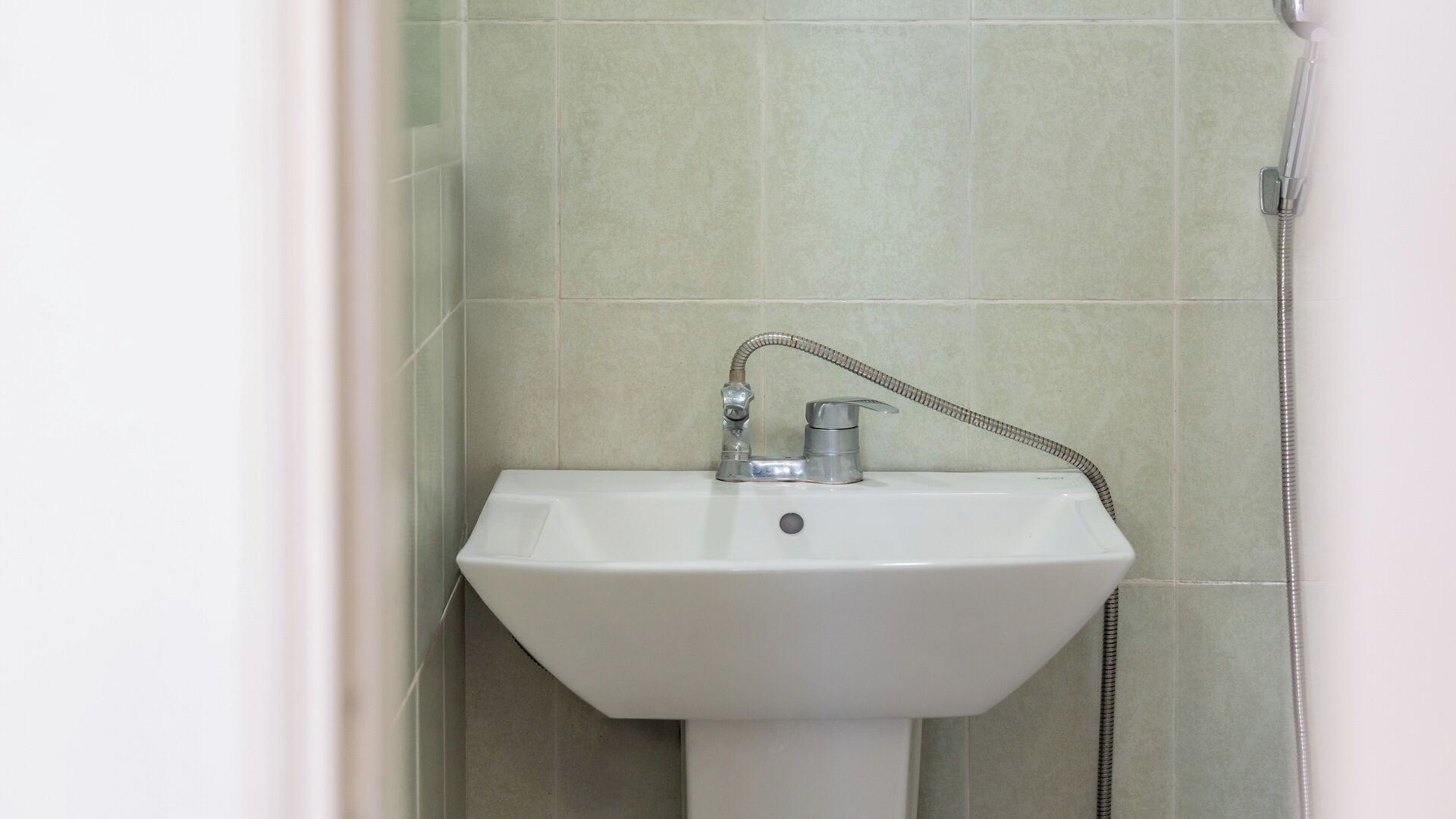 Un baño con lavamanos blanco, ducha de mano y paredes con azulejos.