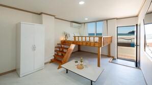 Una habitación pequeña con una cama litera, un armario blanco, una mesita con una botella y un vaso, y vistas a la playa a través de una puerta de cristal.