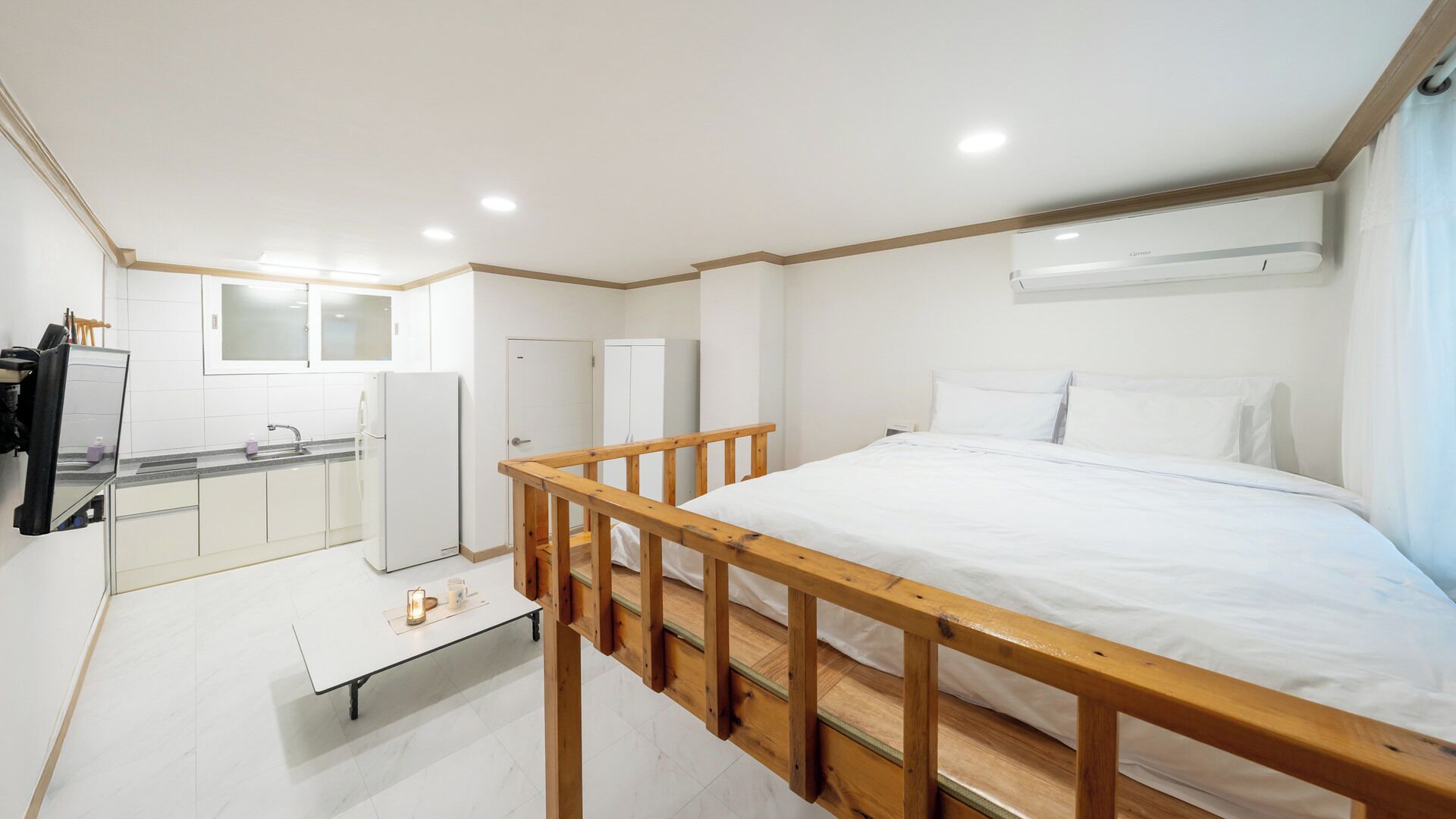 Habitación de hotel compacta con cama, una mesita, kitchenette y baño.