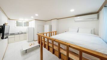 Habitación de hotel compacta con cama, una mesita, kitchenette y baño.