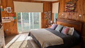 A bedroom with a large bed, wooden walls, a sliding glass door to the outside, and various wall decorations. - CasaBosque minutes from the sea. (Placilla)