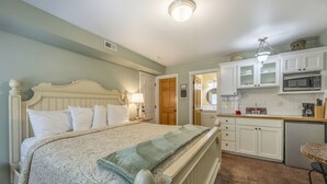 A bedroom with a bed, bedside table, lamp, and a view into the kitchen area. - Private Suite, Hot Tub, Bikes, Fireplace, King Bed, stroll to easy beach access (Depoe Bay)
