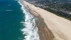 Luchtbeeld van een kustgebied met een zandstrand, oceaan en een stad op de achtergrond.