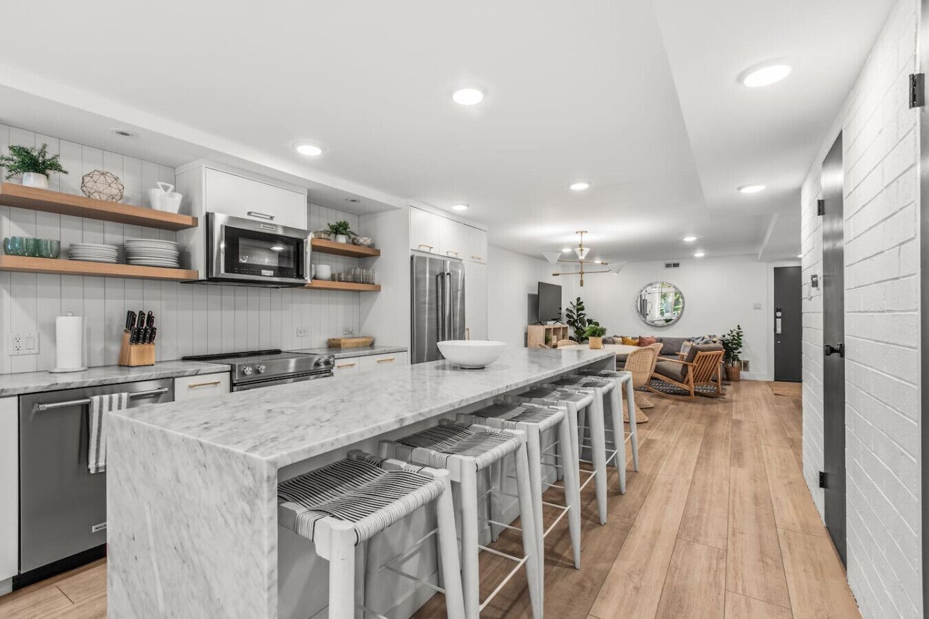 A modern kitchen with a marble island, bar stools, and a dining area with a round mirror.