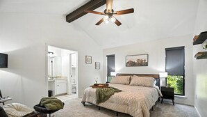 A bedroom with a bed, a chair, a bedside table, a ceiling fan, a window, and a door leading to another room. - The Gathering Place: Near Zoo/Park & Expo Center (Abilene)