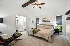 Une chambre à coucher comprenant un lit, une chaise, une table de chevet, un ventilateur de plafond, une fenêtre et une porte donnant sur une autre pièce.