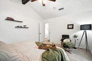 A bedroom with a bed, a chair, a small table, a floor lamp, and a ceiling fan.