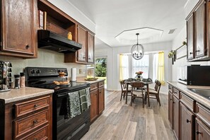 Una cocina con armarios de madera, una estufa negra y un comedor con mesa y sillas.