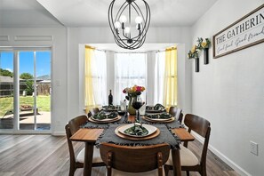 Un coin repas avec une table dressée pour quatre personnes, un lustre et un panneau accroché au mur.