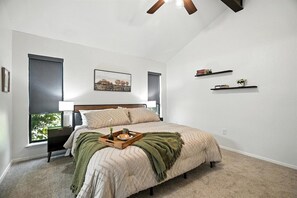 Une chambre à coucher avec un lit, une table de chevet, une fenêtre et un ventilateur de plafond.