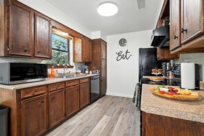 Une cuisine avec des meubles de rangement en bois, un four à micro-ondes, un évier et une horloge murale.