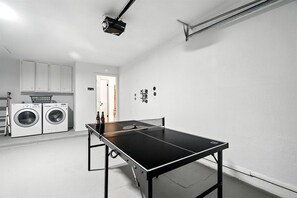 Une pièce équipée d’une table de ping-pong, de machines à laver et d’un projecteur.