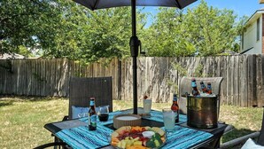 An outdoor patio with a table set for a meal, including a fruit platter, drinks, and a cooler. - The Gathering Place: Near Zoo/Park & Expo Center (Abilene)