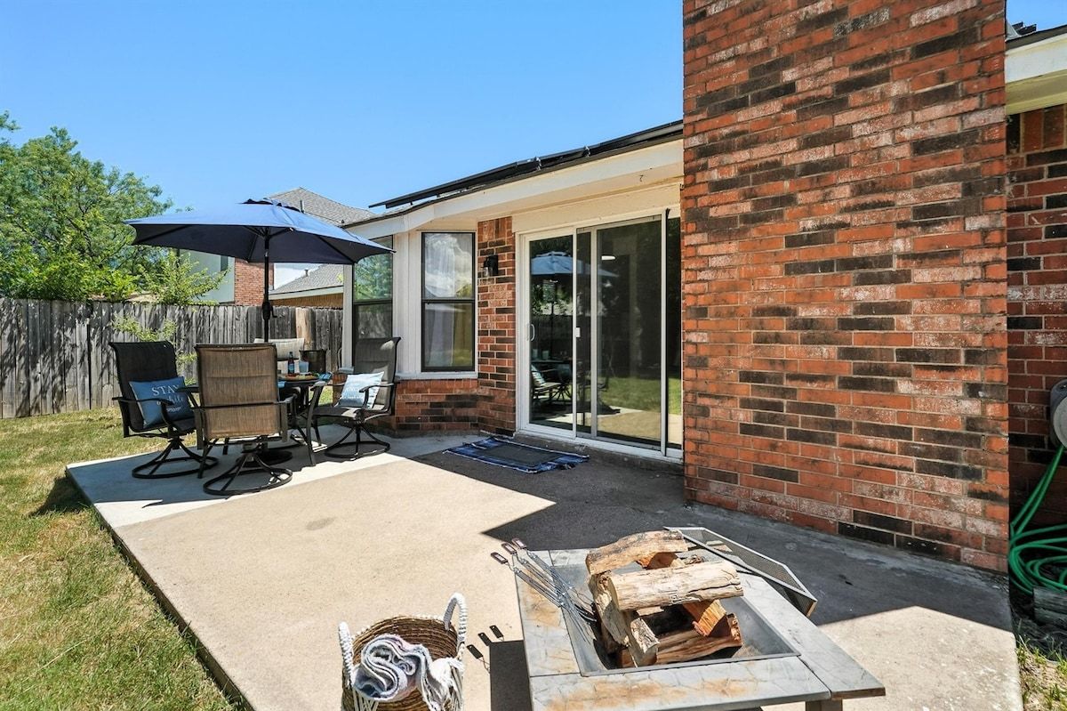 Un espace patio aménagé avec une table et des chaises, un barbecue et une porte-fenêtre coulissante donnant sur un espace extérieur abrité.