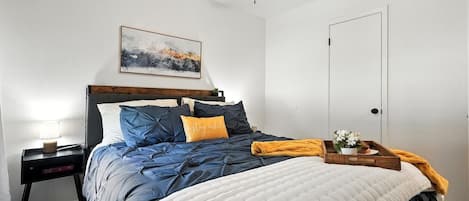 Een slaapkamer met een bed, een nachtkastje, een plafondventilator, een deur en een kunstwerk aan de muur.