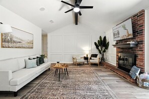 A living room with a white sofa, a coffee table, a fireplace, and a ceiling fan.