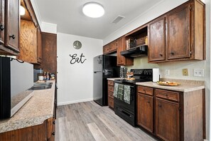 Una cocina con armarios de madera, un refrigerador negro, una estufa y un reloj de pared.