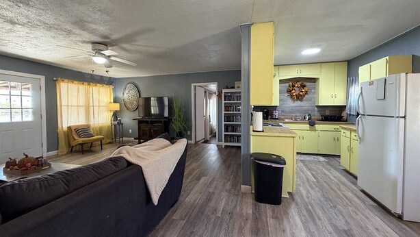 A compact living space with a sofa, a television, and a kitchen area with yellow cabinets and a refrigerator. - Lakeside Hideaway 5-Min to Shackleford AI Site! (Abilene)