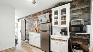 A modern kitchen with white cabinetry, a stainless steel refrigerator, a microwave, and a sign indicating B&B hosting. - Mockingbird Lane – Cozy Rustic Retreat (Abilene)