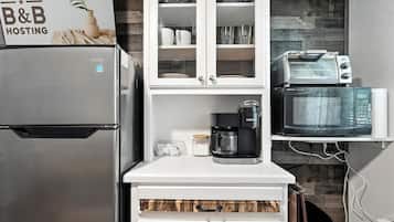 A compact kitchen with a stainless steel refrigerator, a coffee maker, a microwave, and a toaster. There is a cabinet with glass doors above the countertop.