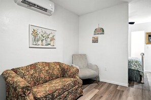 Un salon avec un canapé à motifs floraux, un fauteuil de couleur claire et un climatiseur fixé au mur.