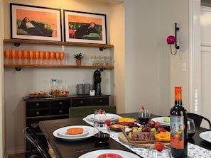 Zona de menjador amb taula preparada per a una posta, amb plats, gots i una ampolla de vi.