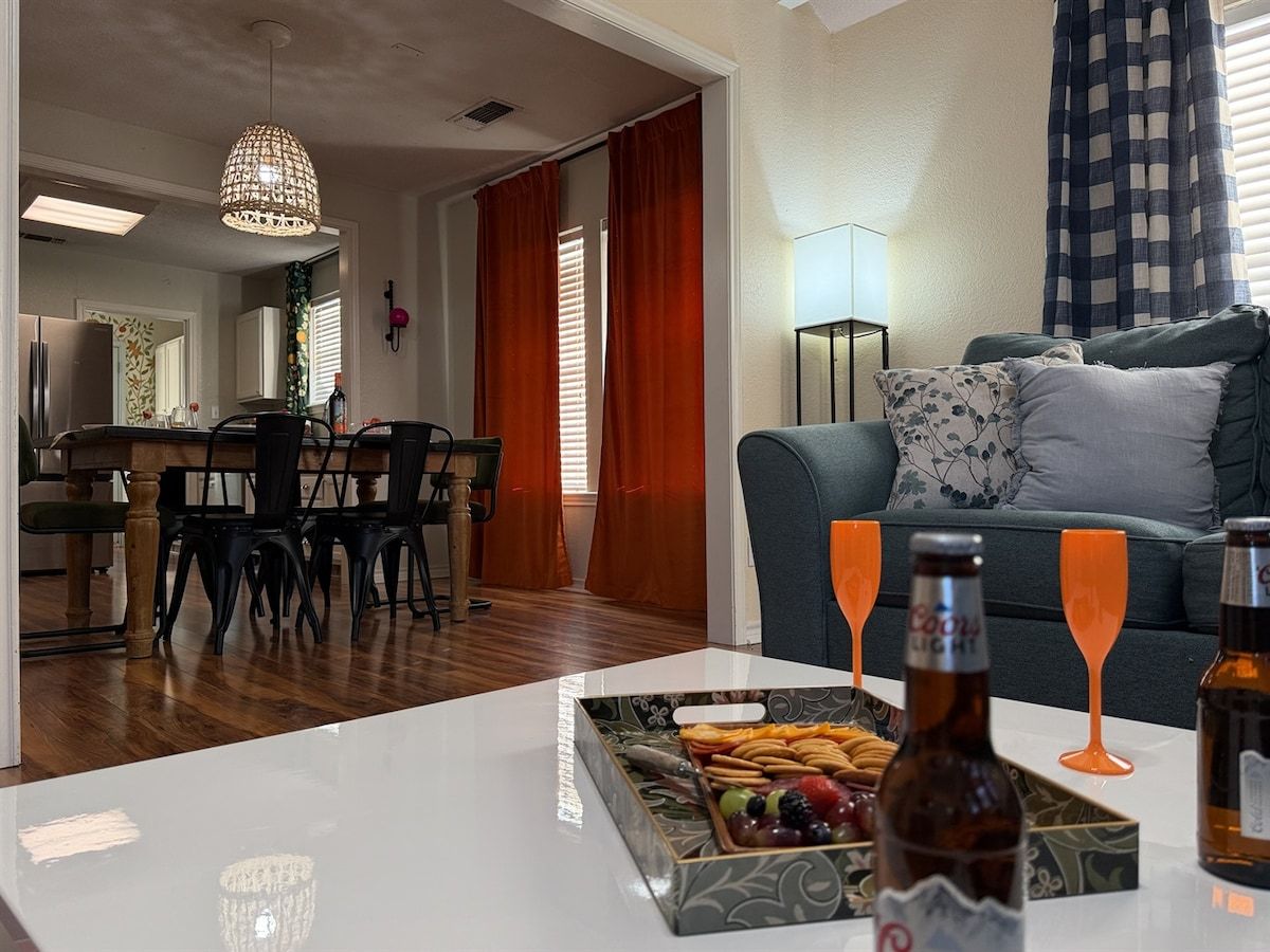 Een woonkamer met een eethoek, een bank en een tafel met lekkernijen en drankjes.
