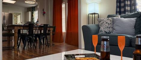 A living room with a dining area, a sofa, and a table with snacks and drinks.
