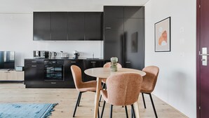 Une cuisine moderne avec des meubles noirs, un coin repas avec une table ronde et quatre chaises, et un tapis bleu sur le sol.