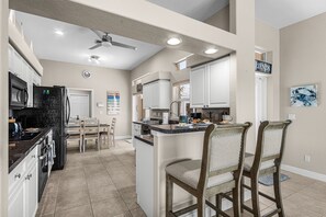 A kitchen with white cabinets, a black refrigerator, and a dining area with wooden chairs. - Waterfront Bliss with Pool & Spa – Your Perfect Escape Awaits - Sunset Cove - Roelens (Cape Coral)