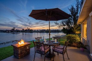 A patio with a fire pit, outdoor table, chairs, and an umbrella. - Waterfront Bliss with Pool & Spa – Your Perfect Escape Awaits - Sunset Cove - Roelens (Cape Coral)