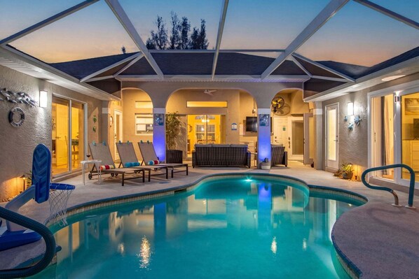 A swimming pool with lounge chairs and a covered patio area. - Waterfront Bliss with Pool & Spa – Your Perfect Escape Awaits - Sunset Cove - Roelens (Cape Coral)