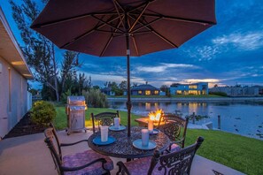 An outdoor patio with a table, chairs, an umbrella, candles, and a grill. - Waterfront Bliss with Pool & Spa – Your Perfect Escape Awaits - Sunset Cove - Roelens (Cape Coral)