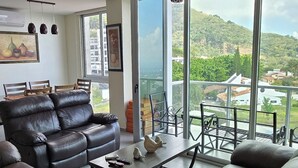 Uma sala de estar moderna com sofás de couro, uma área de jantar e janelas amplas com vista para uma paisagem montanhosa.